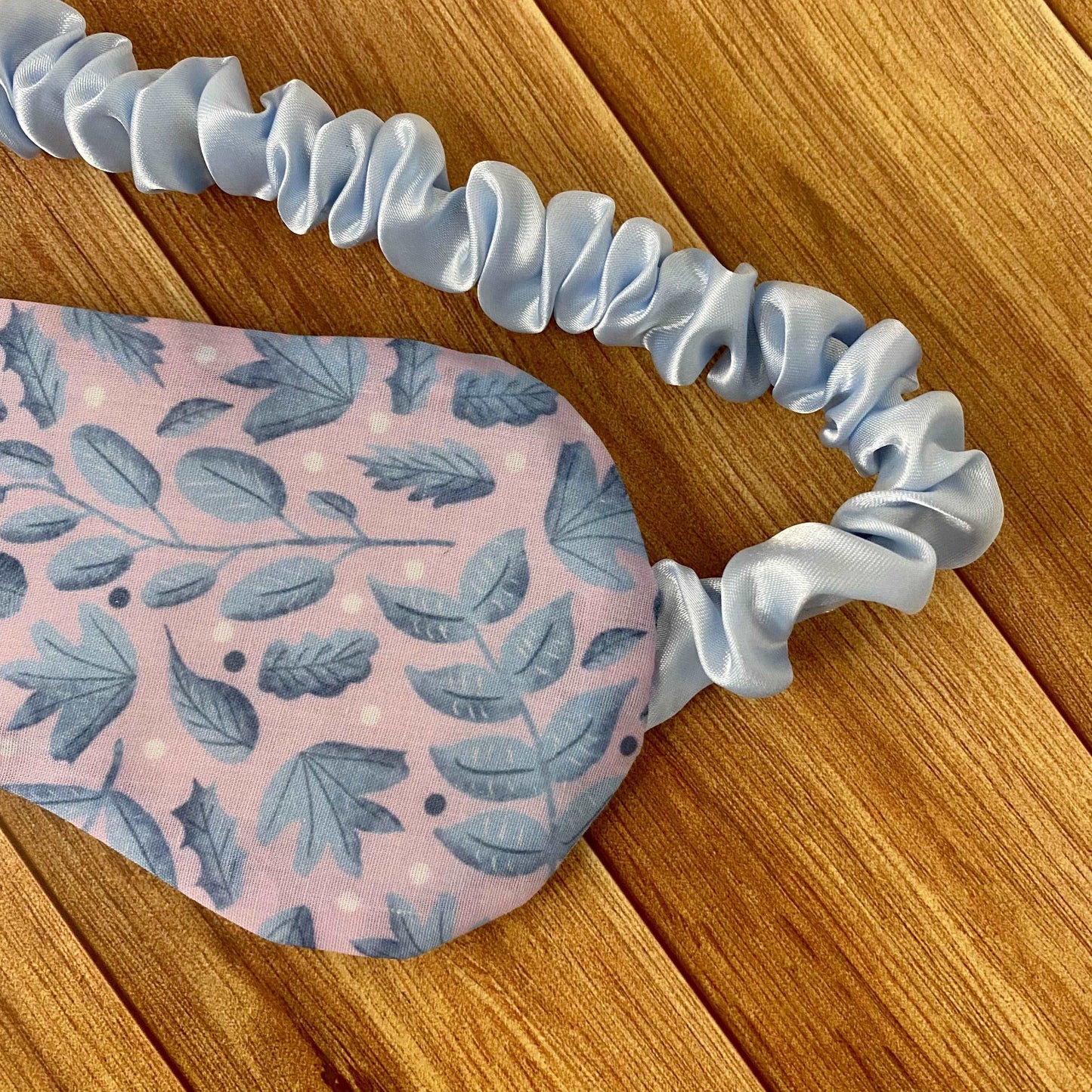 Closeup of blue foliage pattern design on sleepmask with blue strap on a wooden background