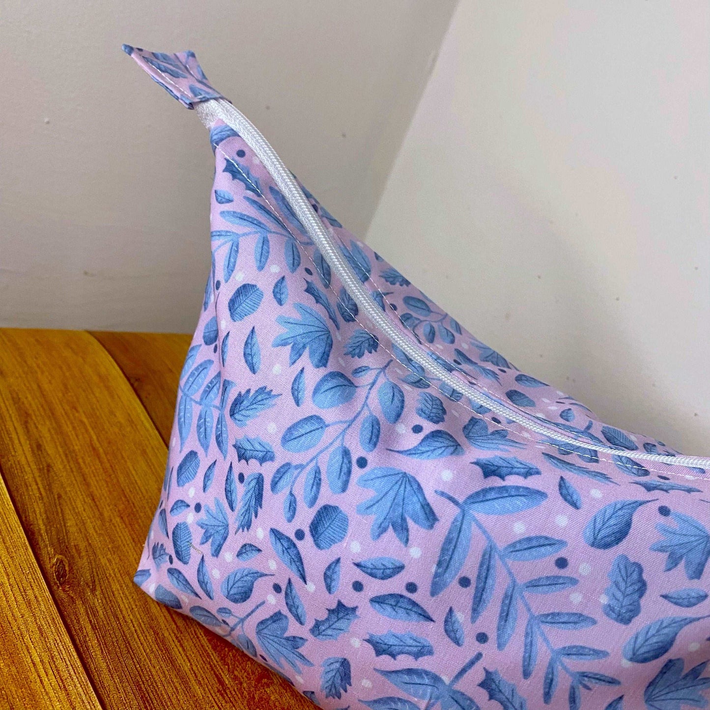 detail of the blue and pink foliage makeup bag, showing the white zip on the top as it sits on a wooden background