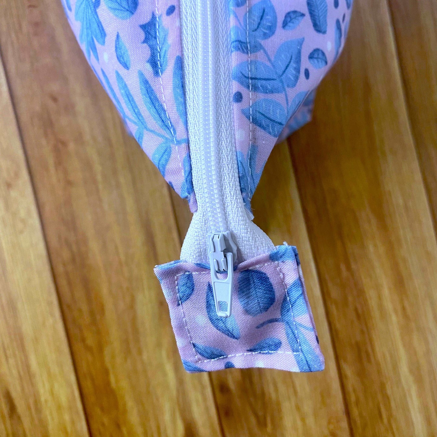Closeup detail of the zip birds eyes view, the blue and pink foliage pattern is on the makeup bag and the zip tag.