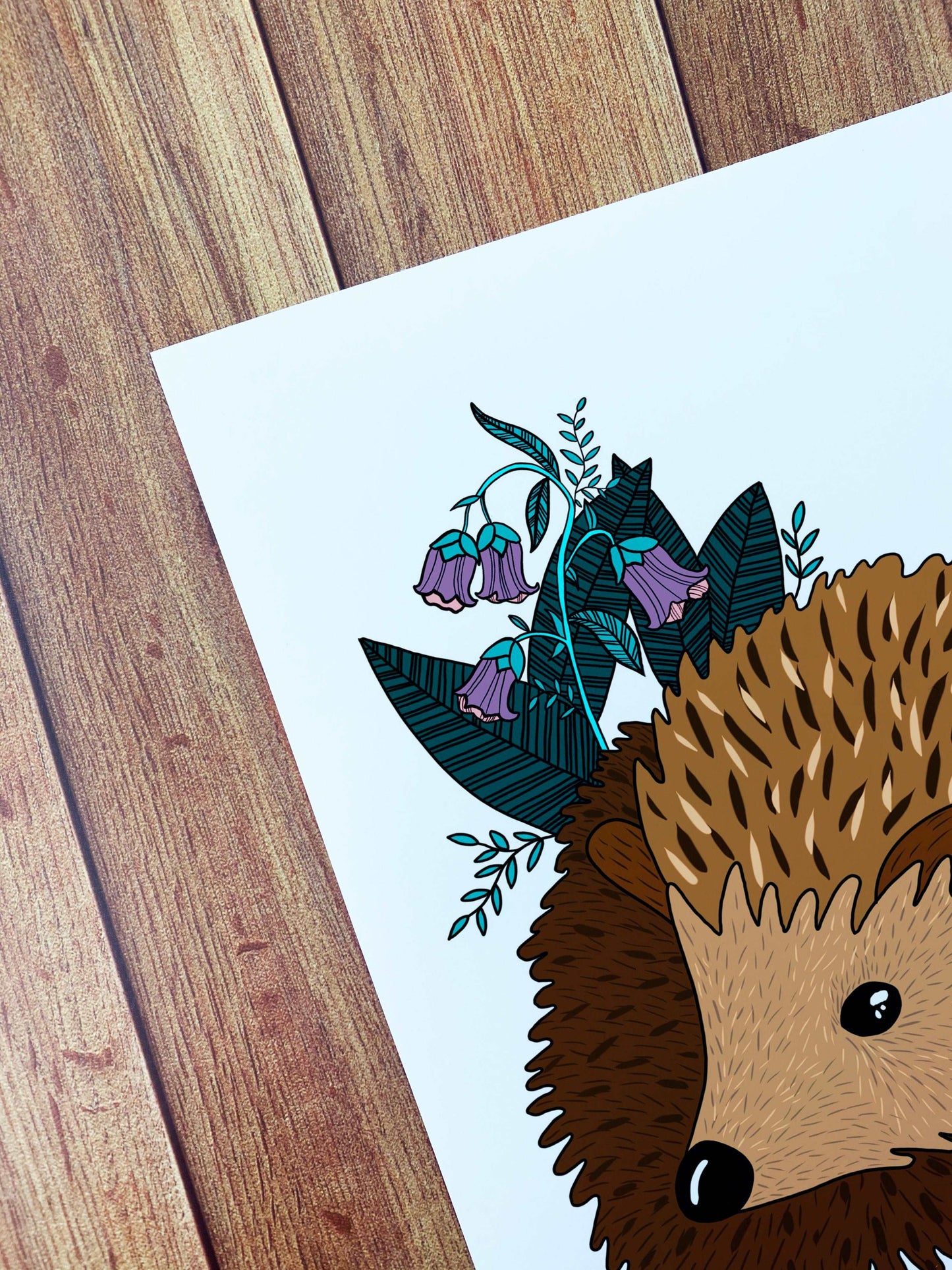 A closeup of the hedgehog print that shows the corner of the print against the wooden background. The print shows a portion of the hedgehog and some of the natural objects behind it