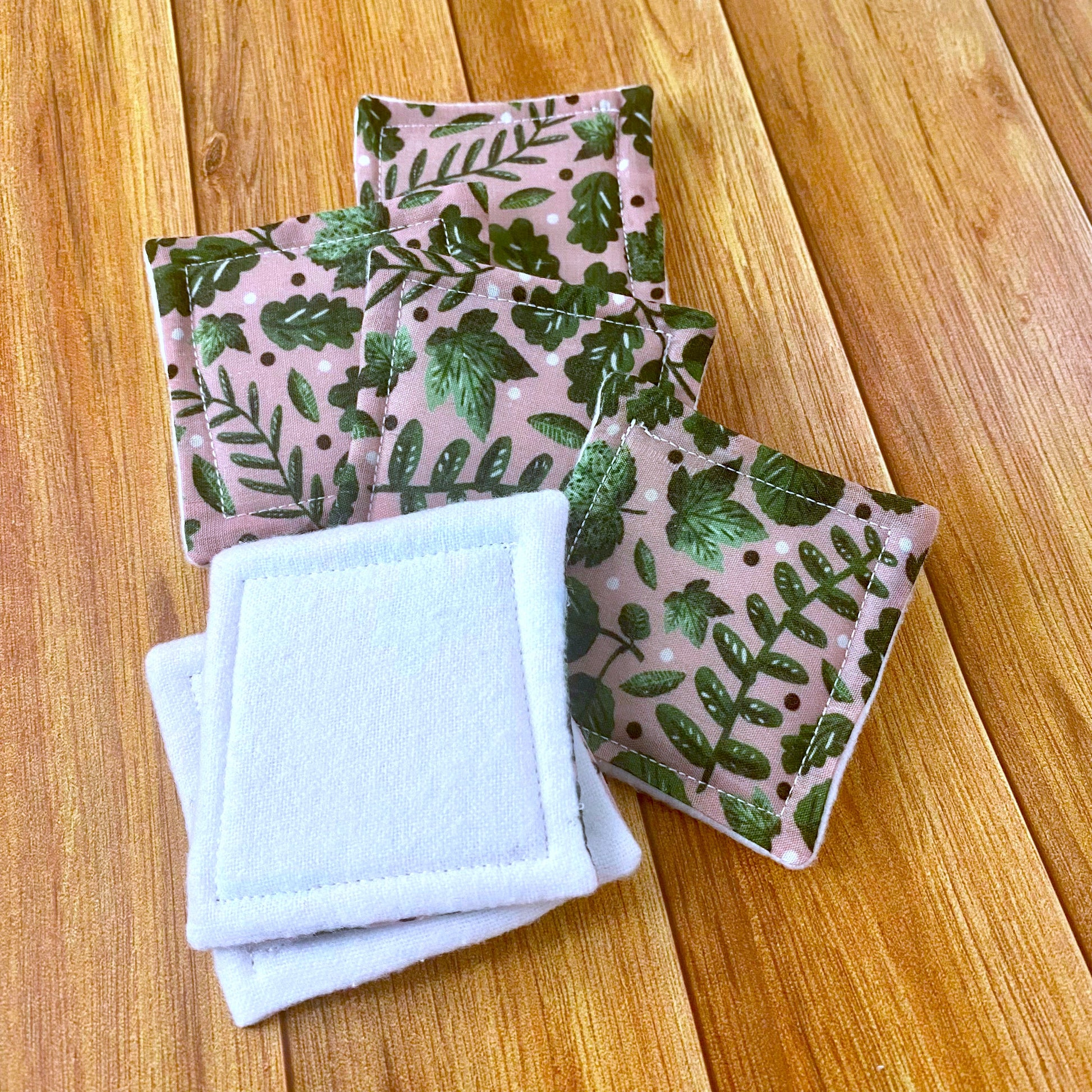 Green foliage patterned skincare pads laid out on a wooden surface, showing two flipped over to the white brushed cotton side