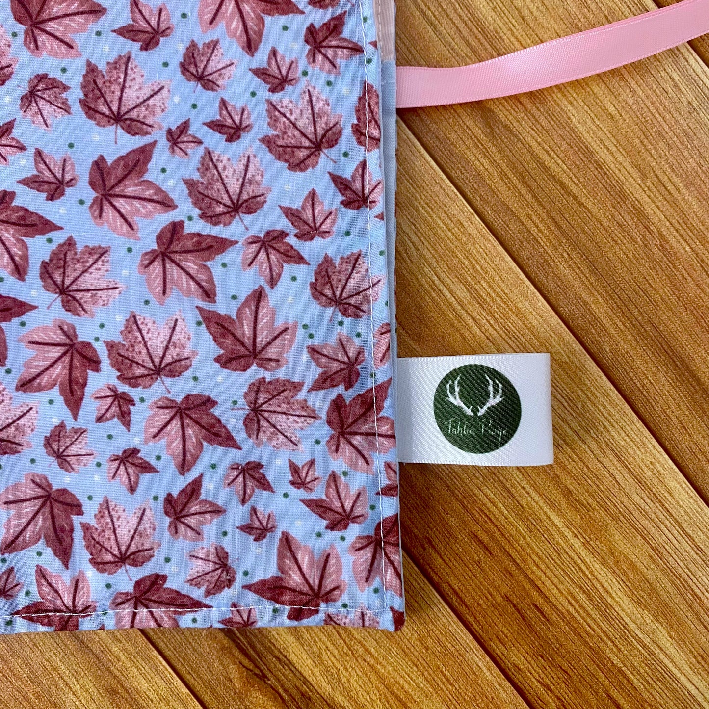 closeup of the corner of the pink leafy brushwrap, the pattern show pink leaves in a graphic style on a blue background. This features on the outside of the brushwrap. The brushwrap is sat on a wooden background.