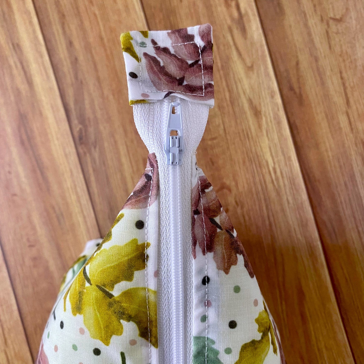 Closeup photograph birds eye view of the pretty foliage makeup bag. This shows the white zip and the square at the end of the zip covered in pattern.