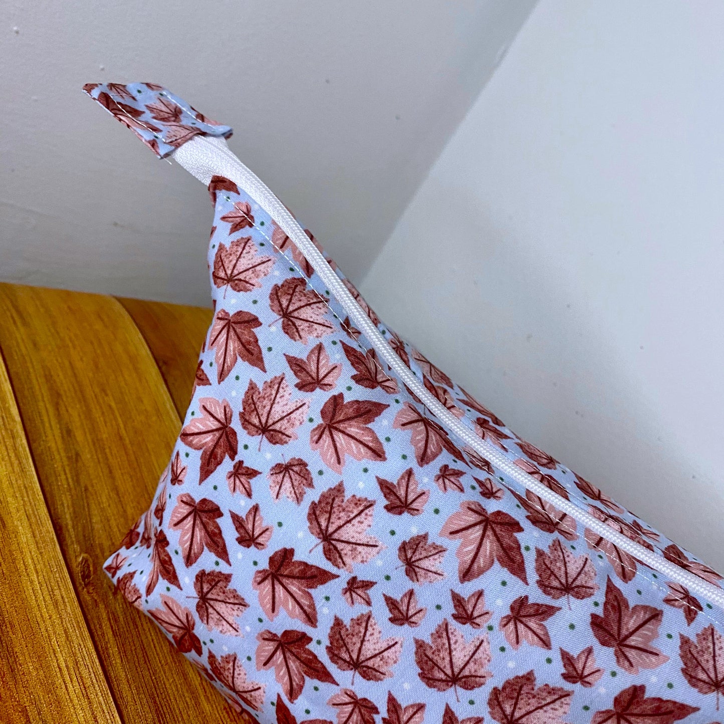 Closeup of the side of the pink leafy patterned makeup bag with a wooden background.
