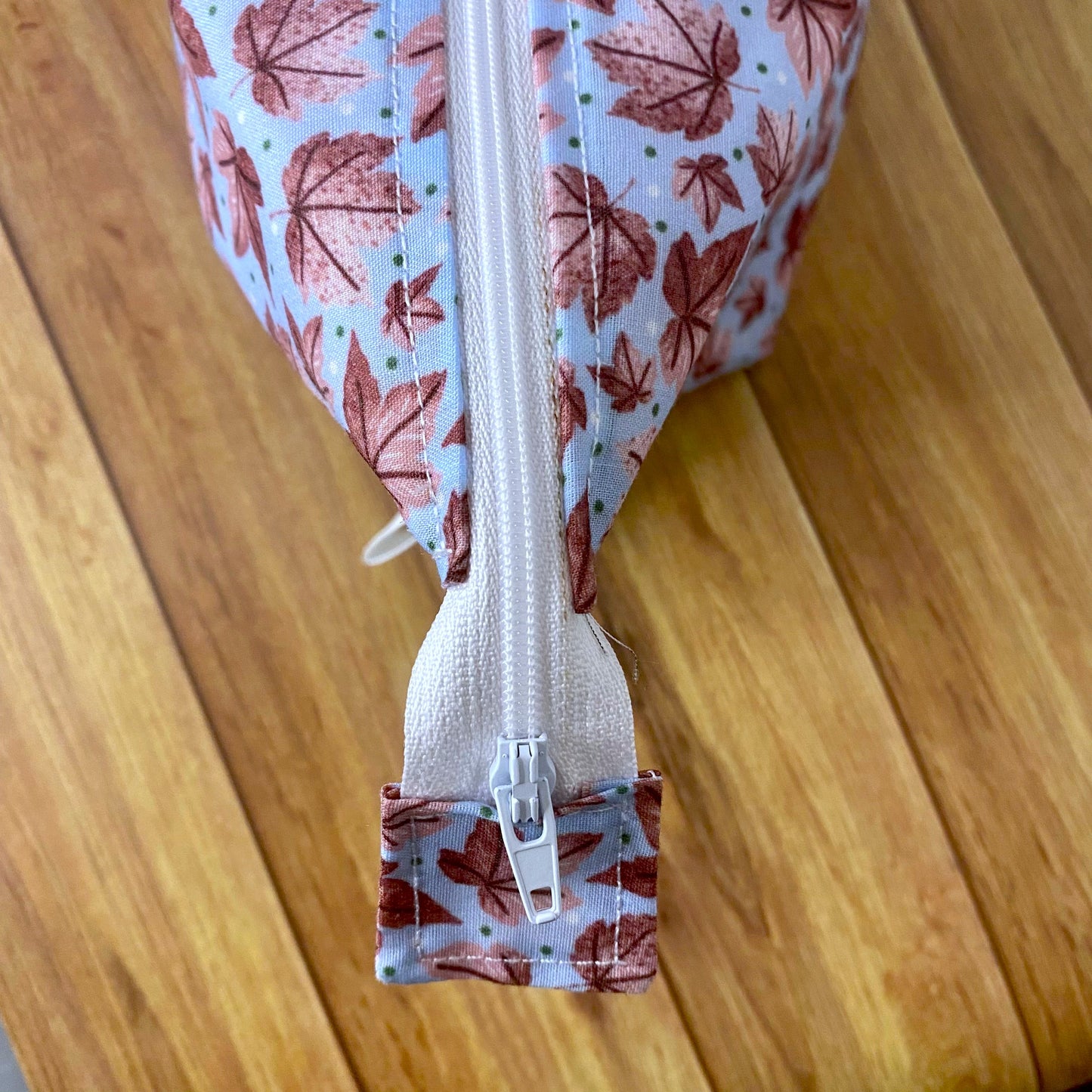 Closeup birds eye view of the pink leafy patterned makeup bag, showing the white zip and the square sewn to the end of it.