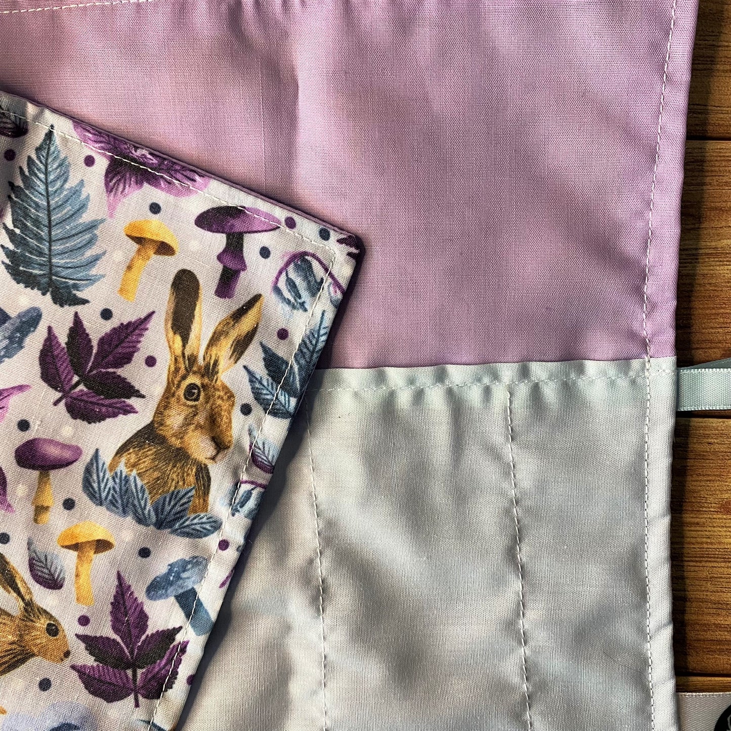 Closeup image of the Hare brushwrap, which shows the inside lilac lining and blue pockets, and a corner of the surface pattern design folded down to show the hares surrounded by purple and blue leaves and mushrooms.