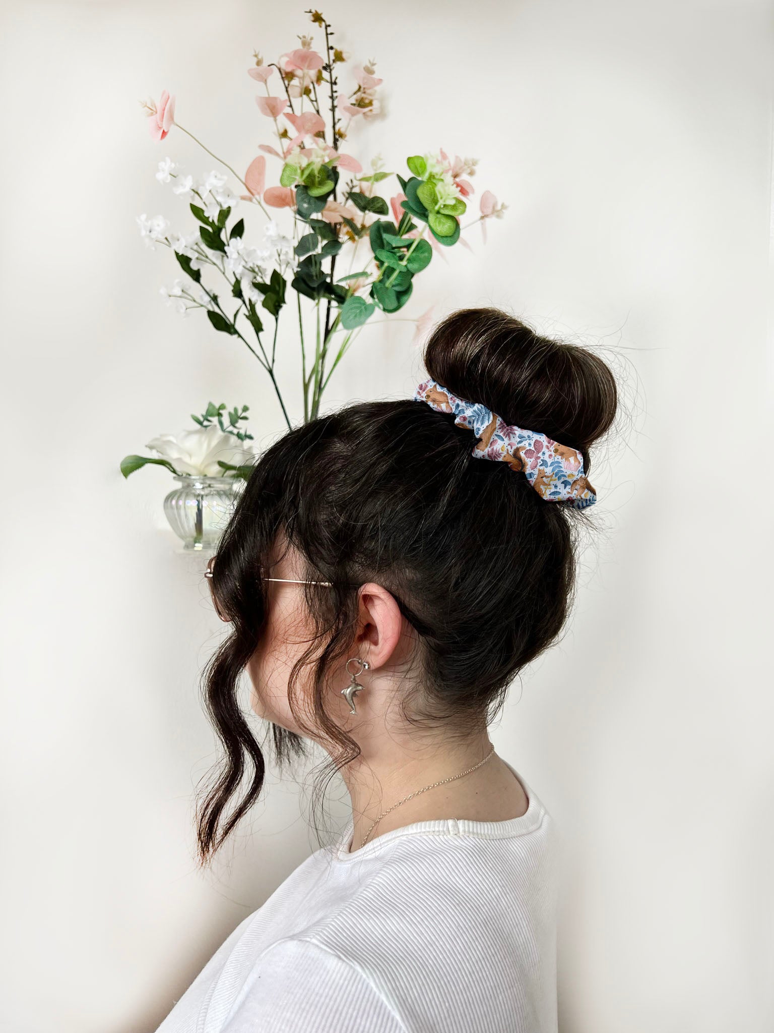 red squirrel scrunchie in back of hair of dark haired girl. She is stood facing sideways with plants behind her.