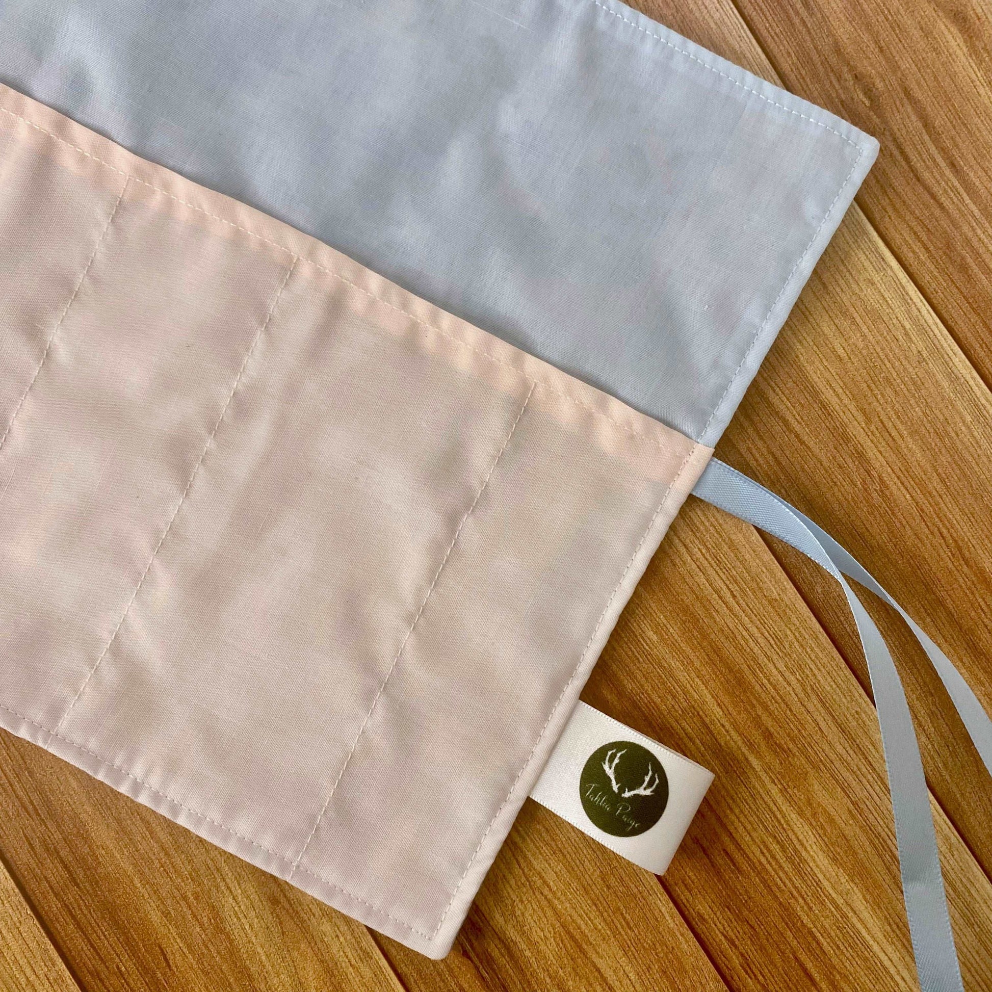 The inside view of the brushwrap showing the plain pink and blue fabrics used to make the backing and the pockets of the wrap. With my Tahlia Paige label sewn onto the side and some blue ribbon. Lying on a wooden background