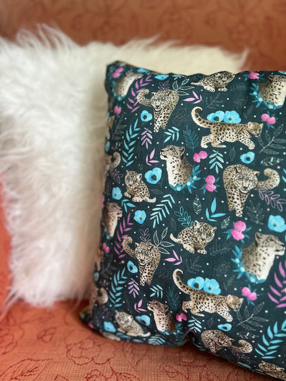 Closeup of snow leopard cushion, with a white cushion behind it on a  pink armchair. This cushion is an ideal gift for a wild animal lover.