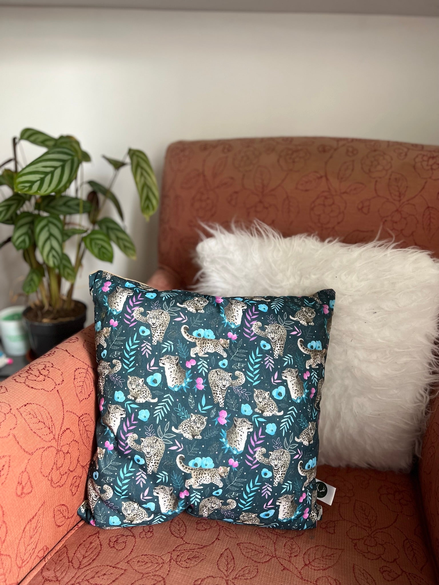 snow leopard cushion on a pink armchair, a great wild animal gift for someone who loves endangered species.