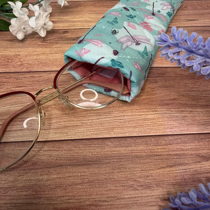 Quilted fabric glasses pouch featuring a dragonfly pattern and secure fastening.
