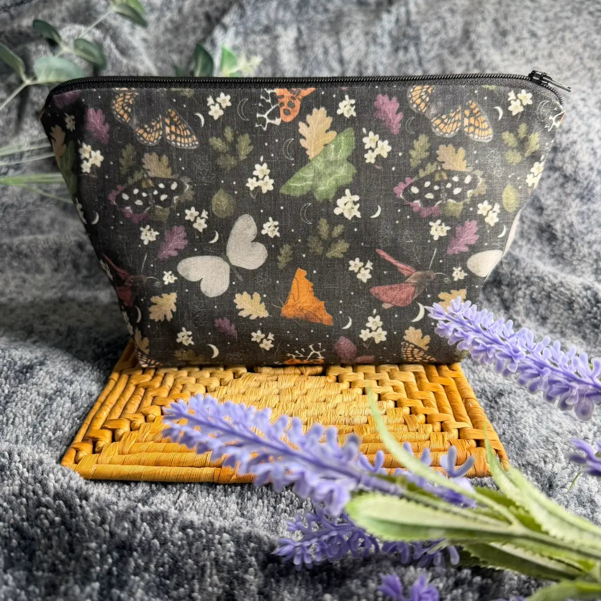 Black makeup bag with a repeating moth pattern and white waterproof nylon lining.
