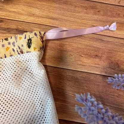 Small white netted laundry wash bag with a patterned bee fabric top.
