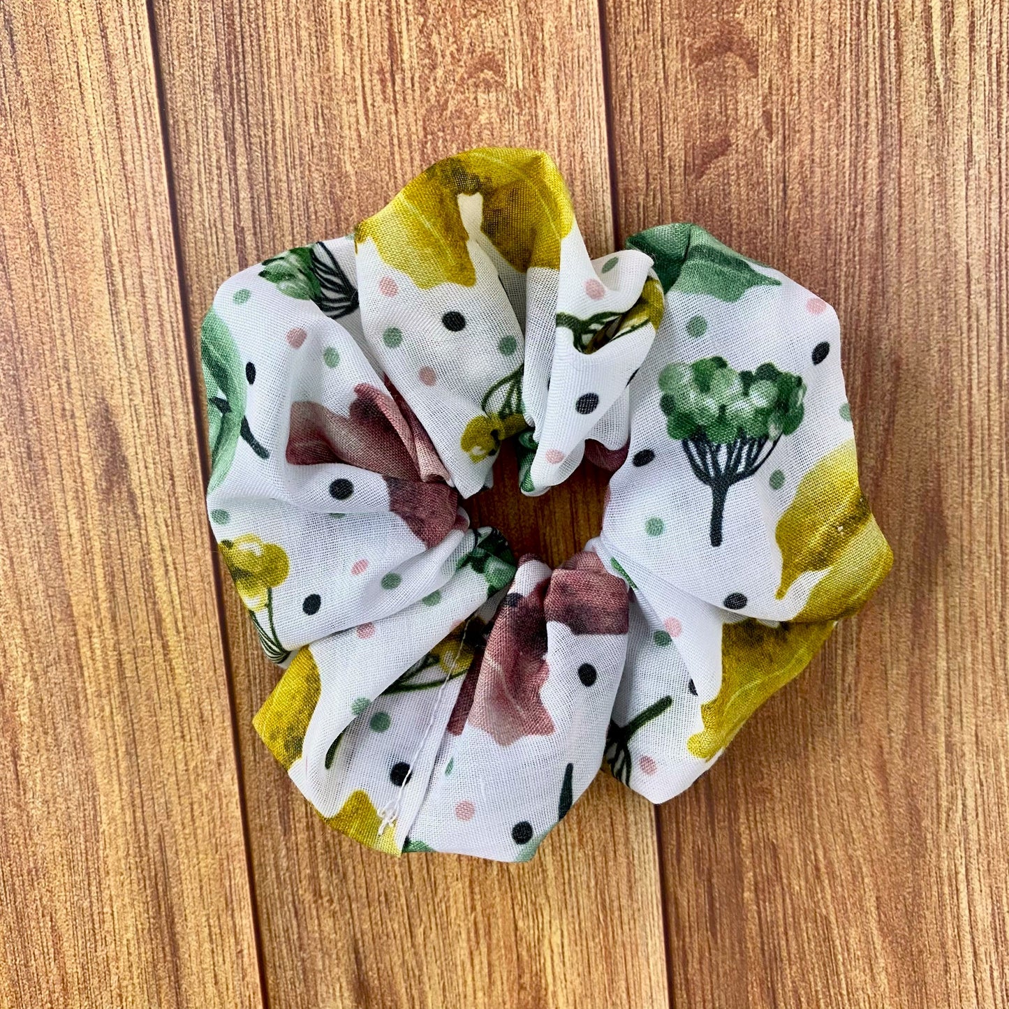 photograph of scrunchie on wooden background, it has a white fabric with colours in the pattern