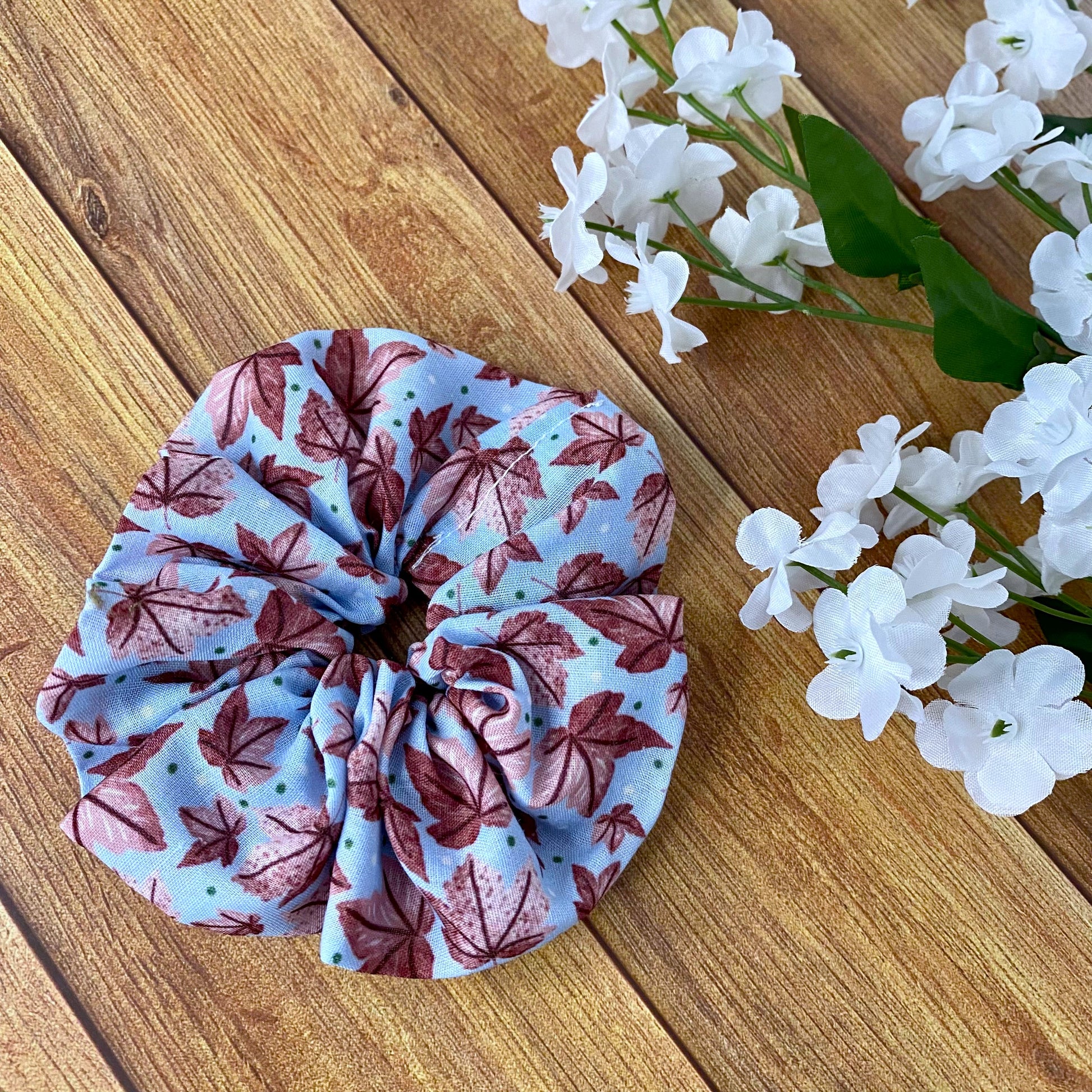 pink leafy patterned scrunchie on wooden background with flowers around it