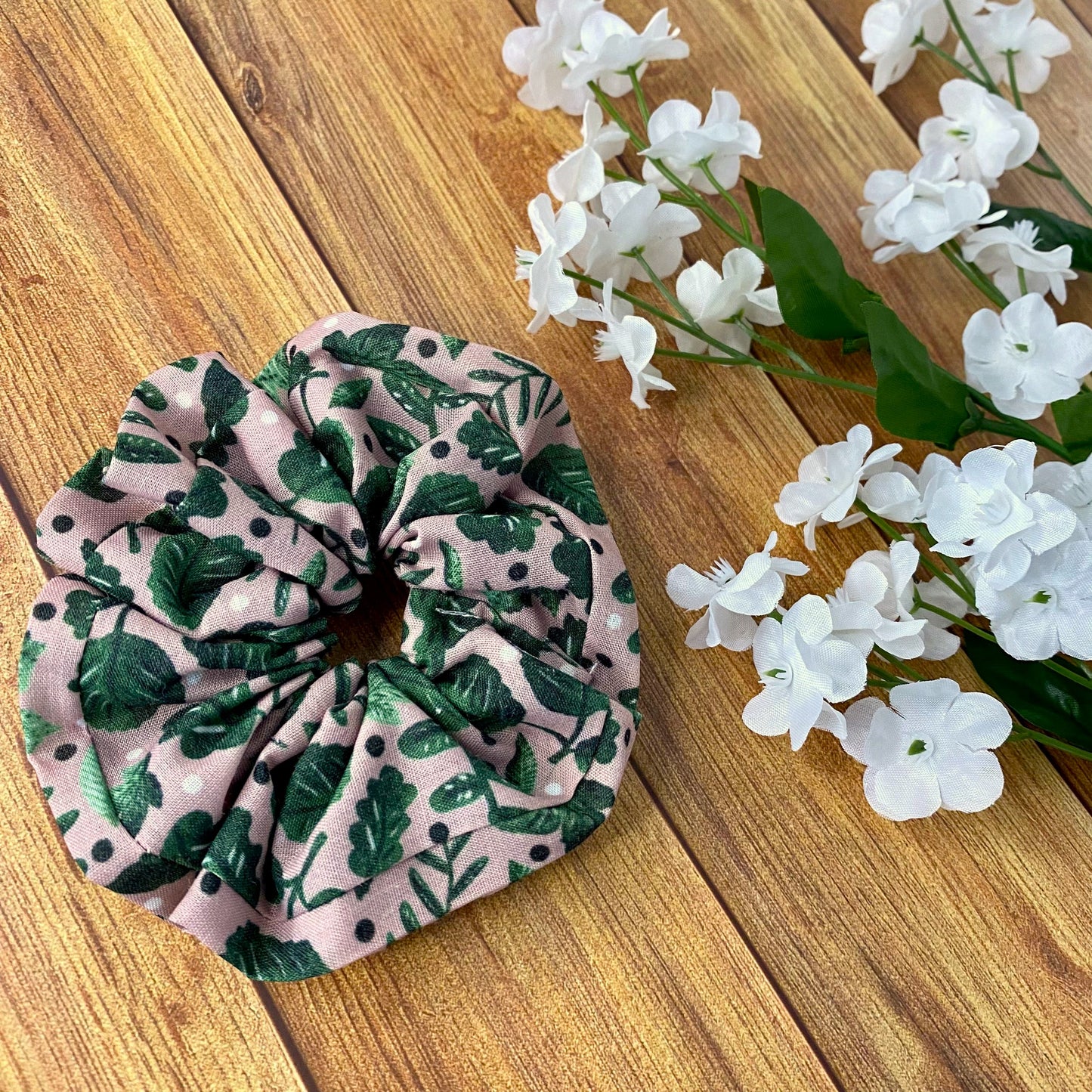 green foliage scrunchie sat on wooden background with white flowers around it