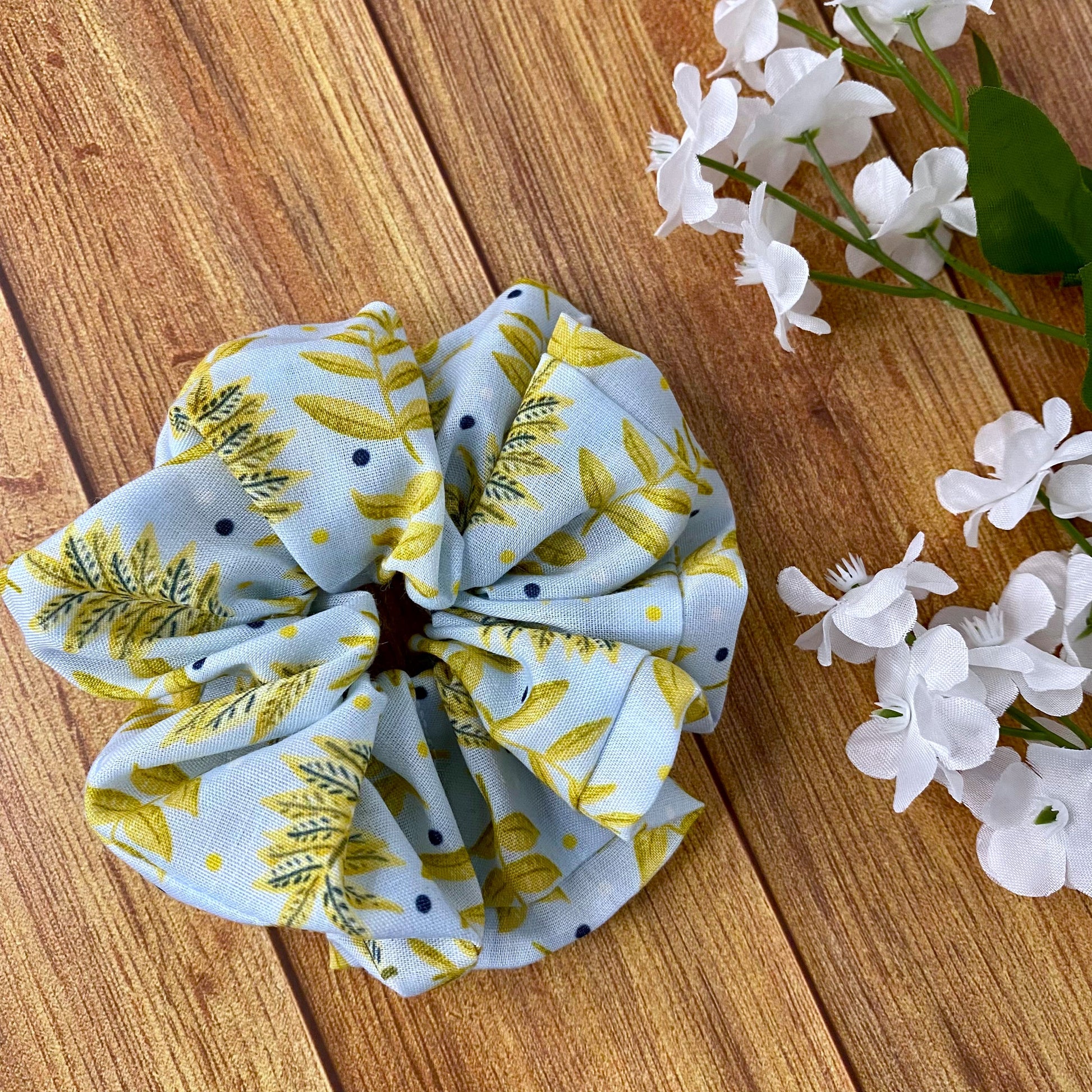 yellow foliaged patterned scrunchie on wood surface with flowers around it