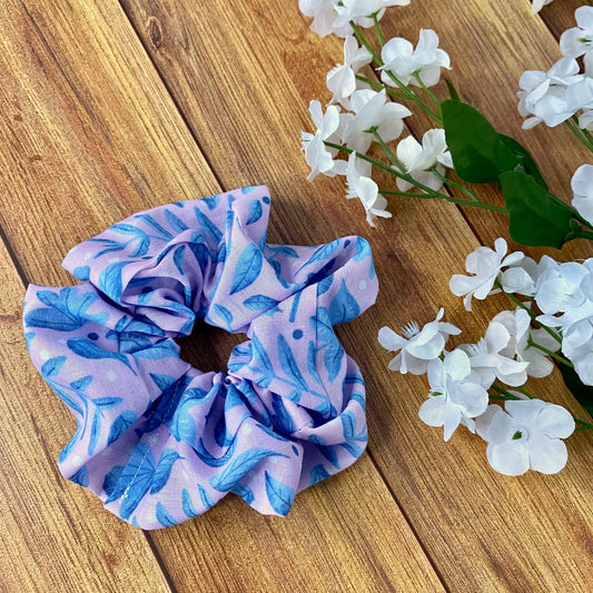 blue foliage on pink surface pattern design on a scrunchie, shown on a wooden background with white flowers