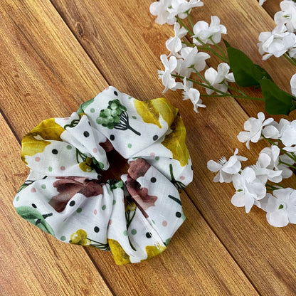 Pretty foliage patterned white scrunchie on a wooden backdrop with flowers around it