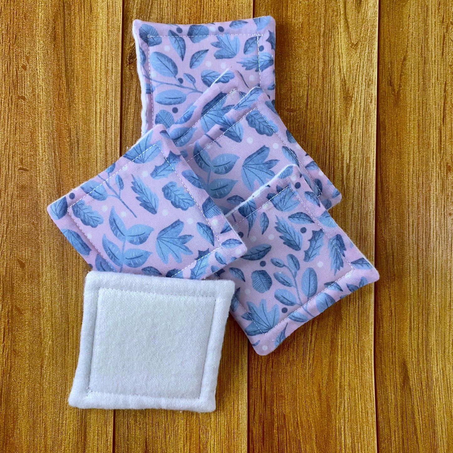 six reusable skincare pads in a pile showing the blue and pink foliage pattern on five and the white brushed cotton on the one at the front, all on a wooden background