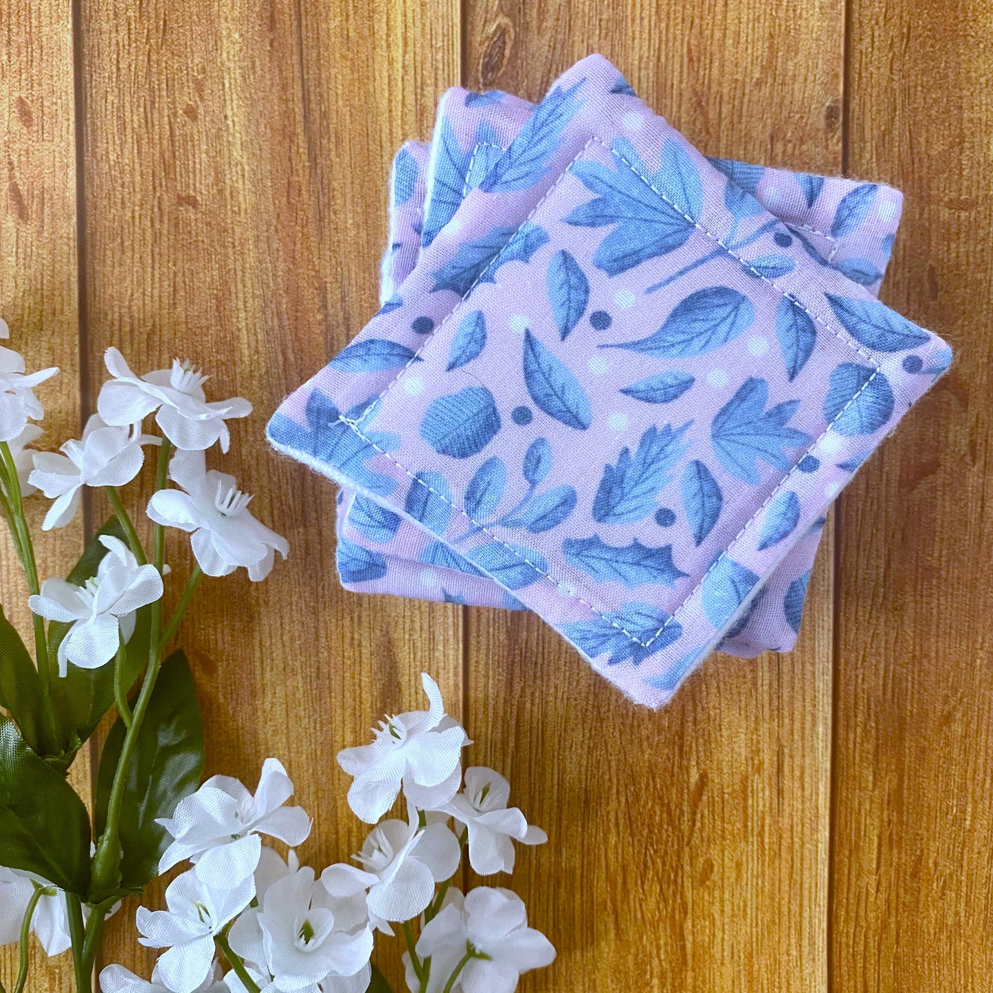 blue and pink foliage pattern on square skincare pads in a pile next to some flowers on a wooden background