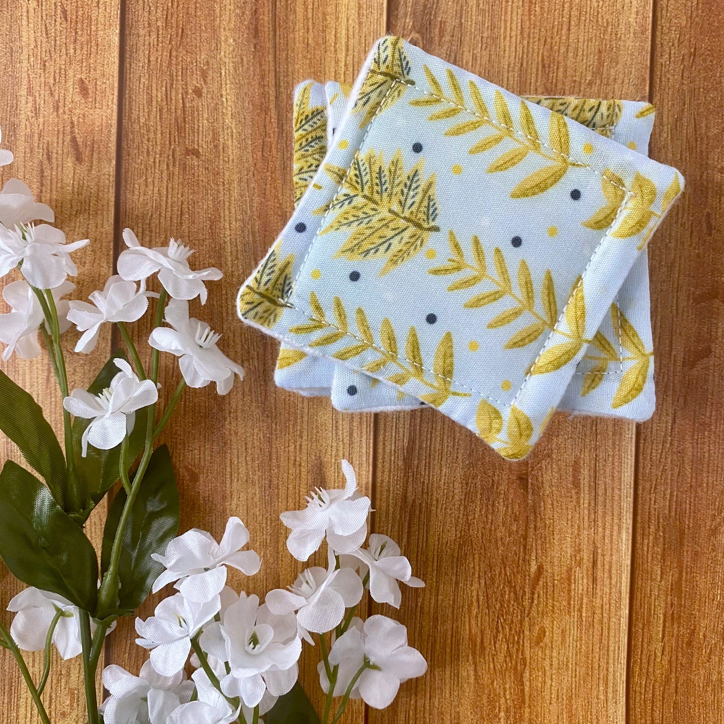 yellow foliage patterned reusable skincare pads in a stack next to some flowers, all on a wooden background