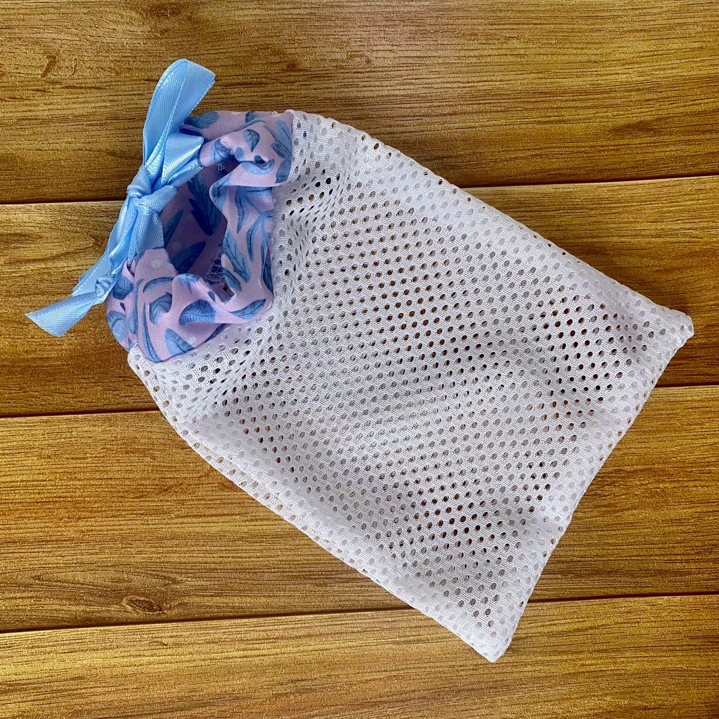 blue and pink foliage pattern on the top of a white mesh washbag, on a wooden background