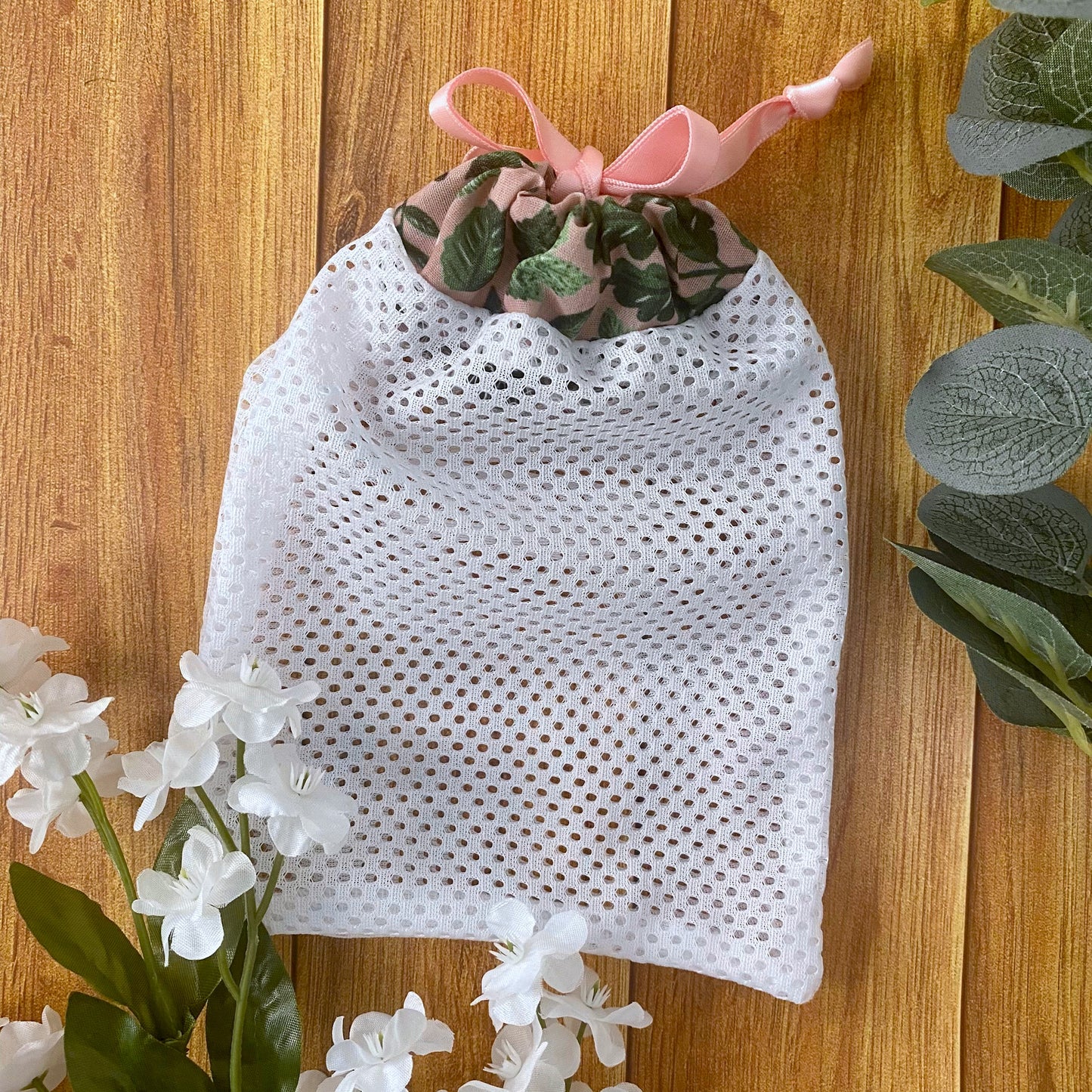 green foliage patterned washbag with white mesh on a wooden background