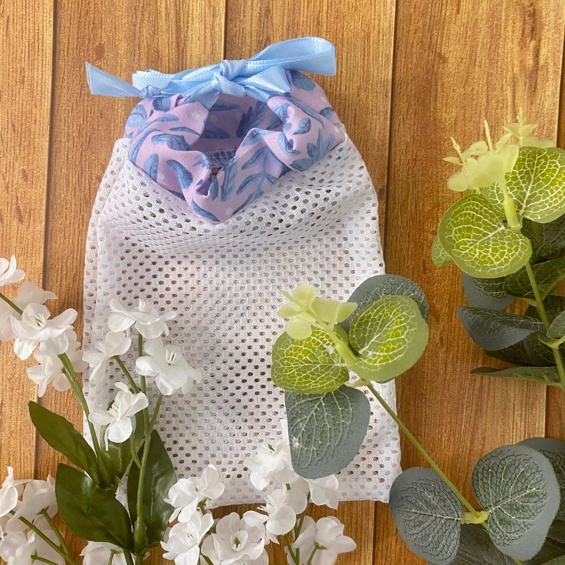 blue and pink foliage pattern on the top of a white mesh washbag amongst the green and white foliage