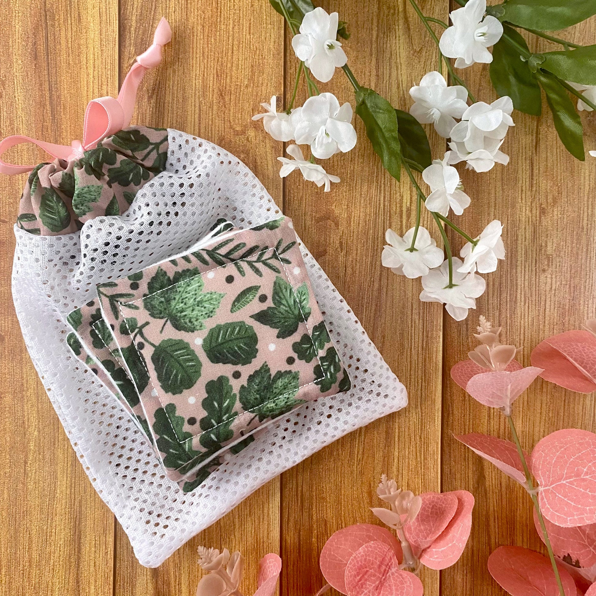 green foliage patterned reusable skincare pads and washbag on wood surface with flowers around them