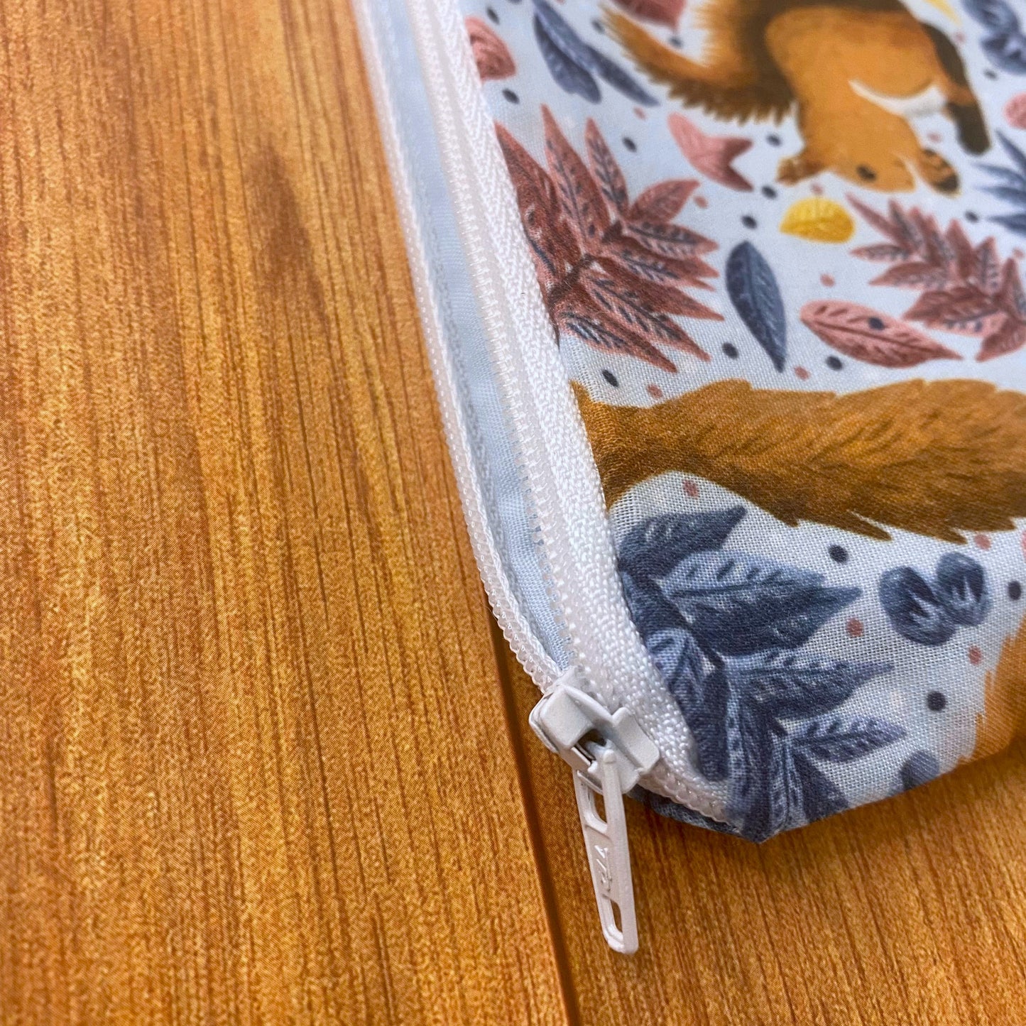 Closeup of white zip on the corner of the red squirrel patterned pouch, ideal as a red squirrel gift.