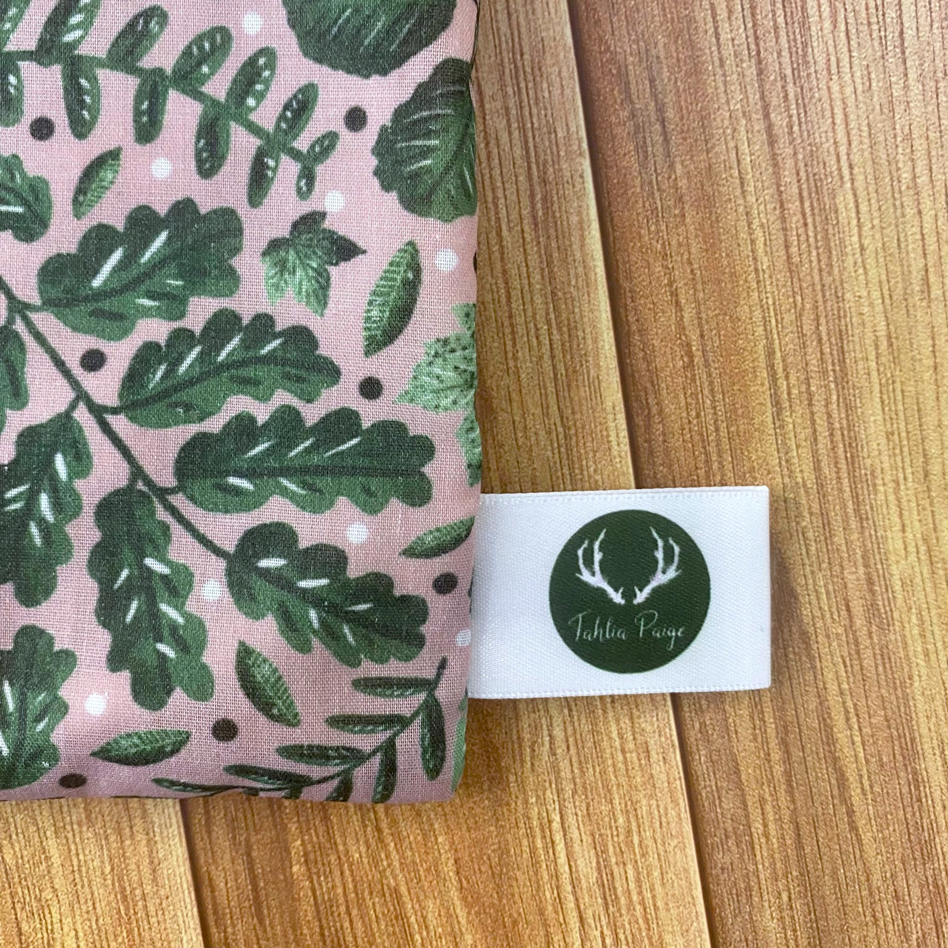 closeup of cosmetic bag gift showing the brand tag, and the green foliage pattern on the fabric. Ideal for a nature lover, this storage pouch is ideal for skincare storage.