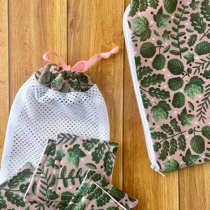 closeup of reusable pads, washbag and pouch on wooden surface, the giftset all has the green foliage pattern on it