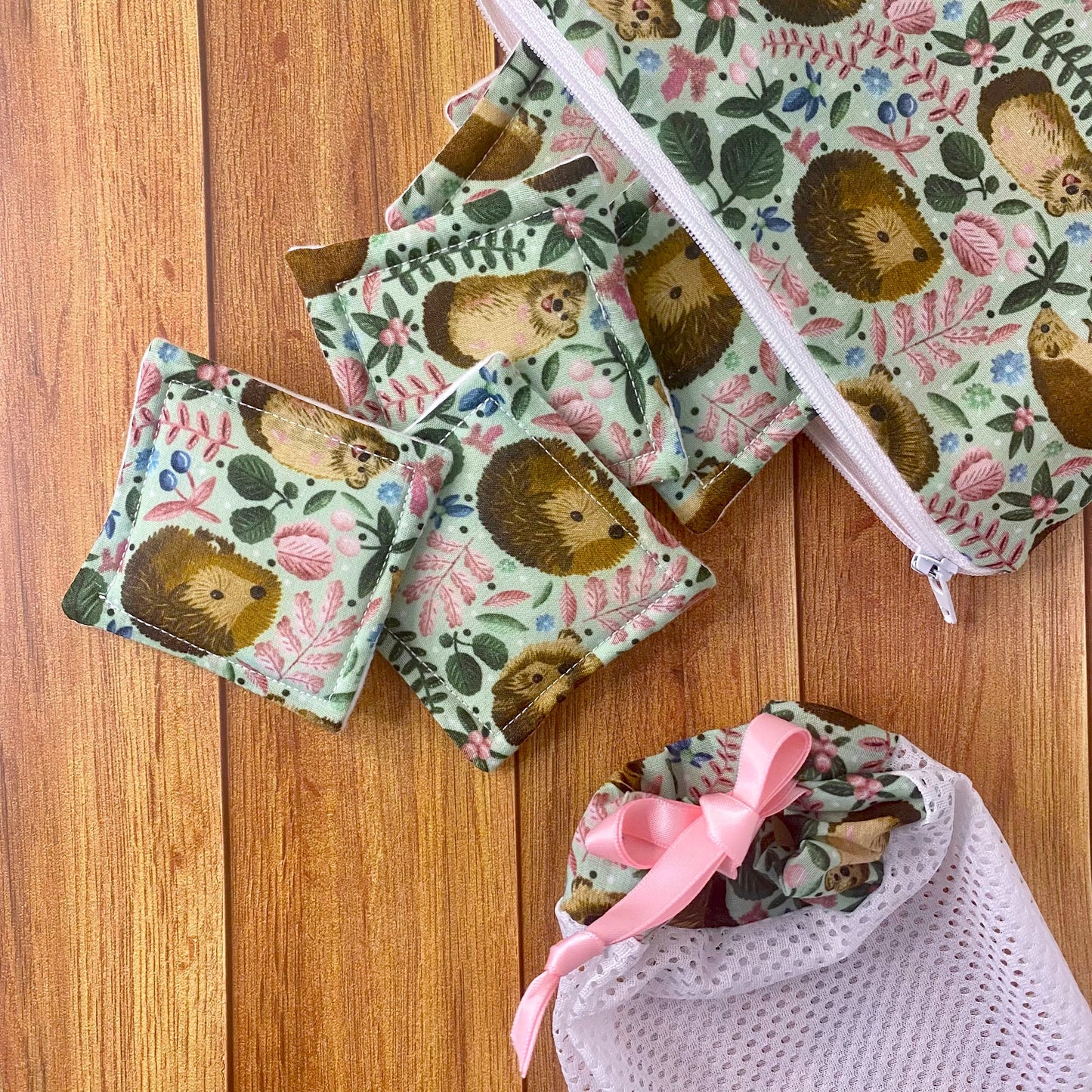 hedgehog patterned reusable skincare pads spilling out of a hedgehog patterned pouch and a matching washbag nearby on wooden surface