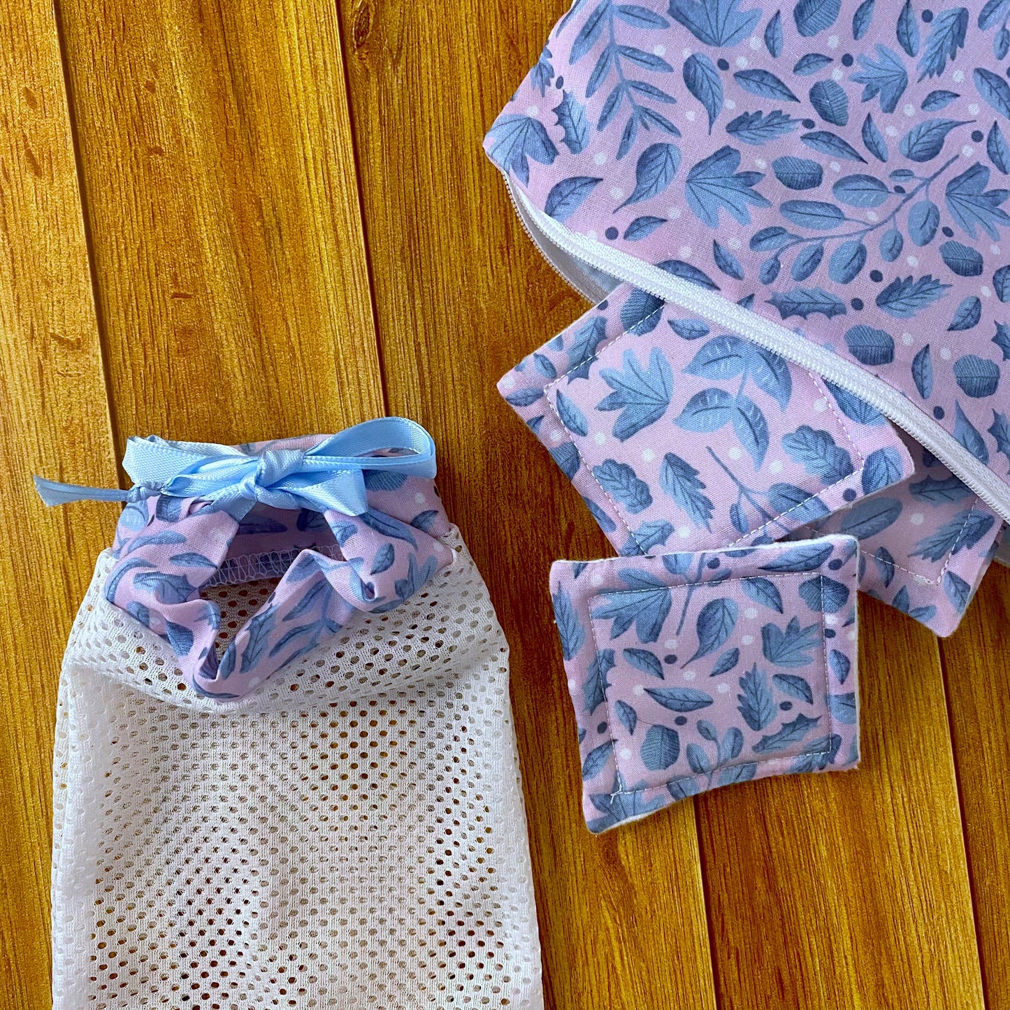 reusable skincare pads coming out of a pouch with a washbag next to them, all in a blue foliage pattern with a wooden background