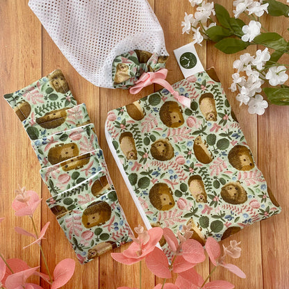Hedgehog patterned giftset on wooden surface with foliage around it. Giftset includes hedgehog patterned pouch, reusable skincare pads and washbag arranged on wood surface here.
