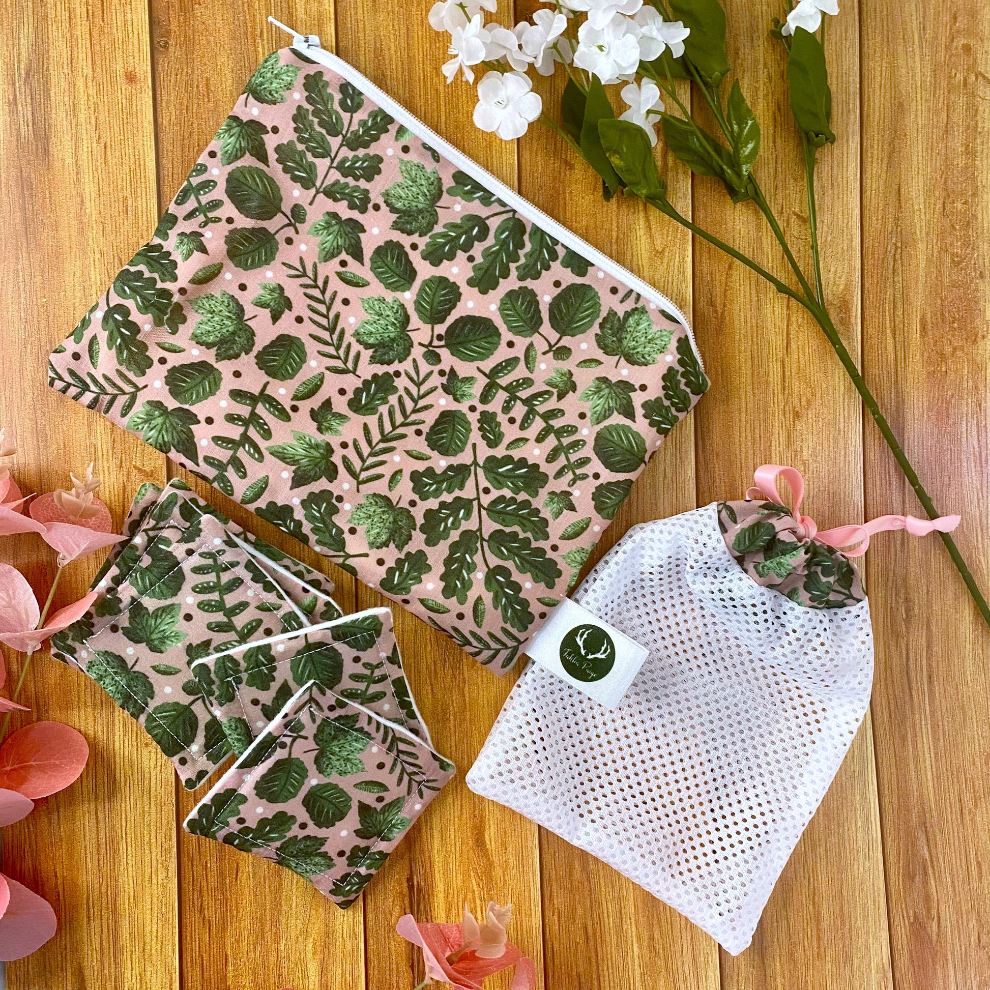 green foliage patterned pouch, reusable skincare pads and washbag all matching, on a wooden backdrop with flowers around them
