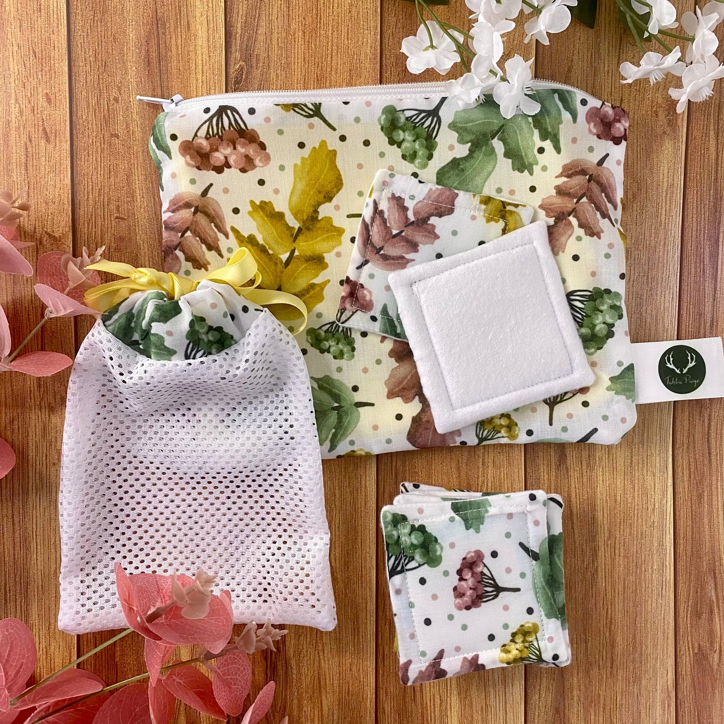 pretty foliage patterned pouch, reusable makeup removal pads and washbag on wooden background with foliage around it
