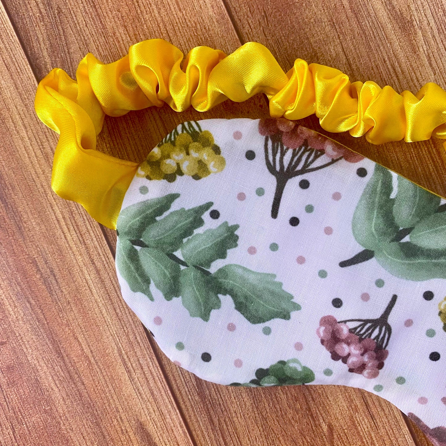 closeup of front of sleepmask showing white pattern with foliage and yellow scrunched satin strap