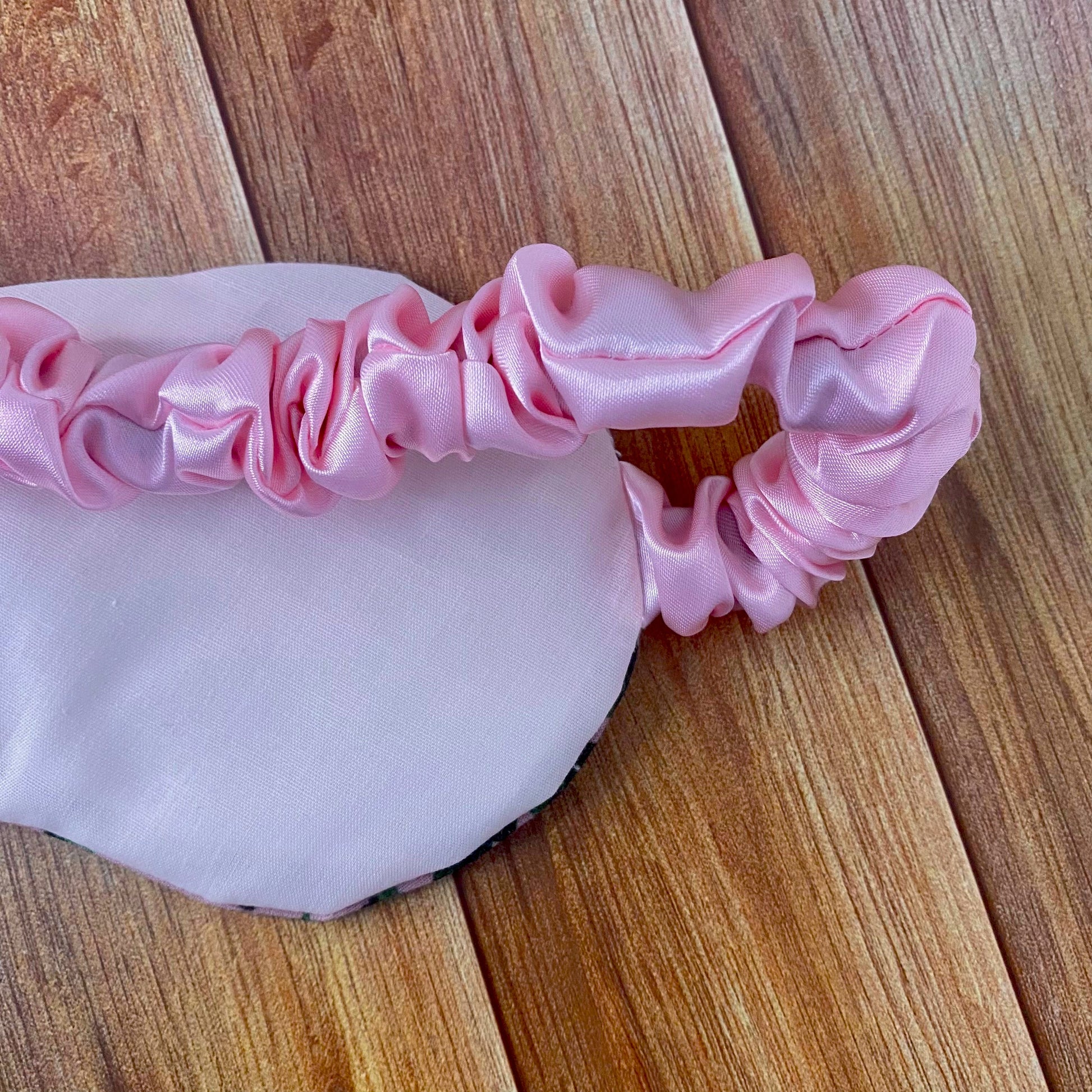 green foliage sleepmask back shown on a wooden background, showing pink backing and pink strap