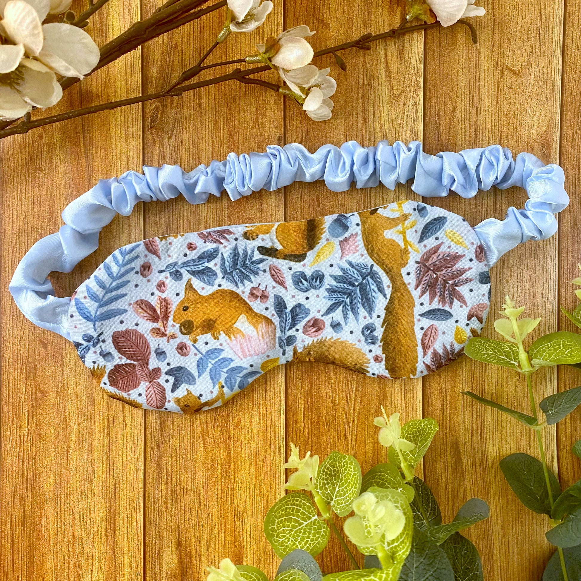 red squirrel patterned sleepmask on wooden backdrop with foliage around it