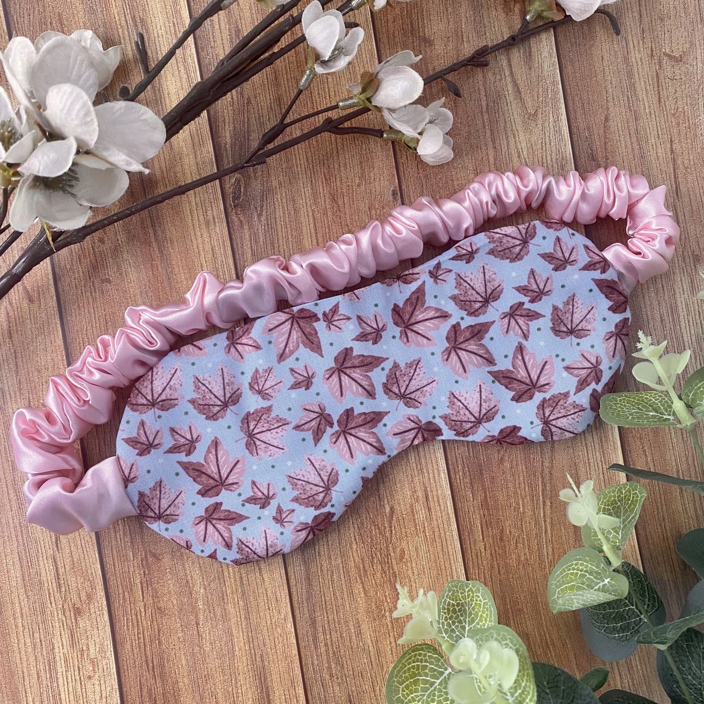 pink leafy patterned sleepmask on wooden background and foliage around it