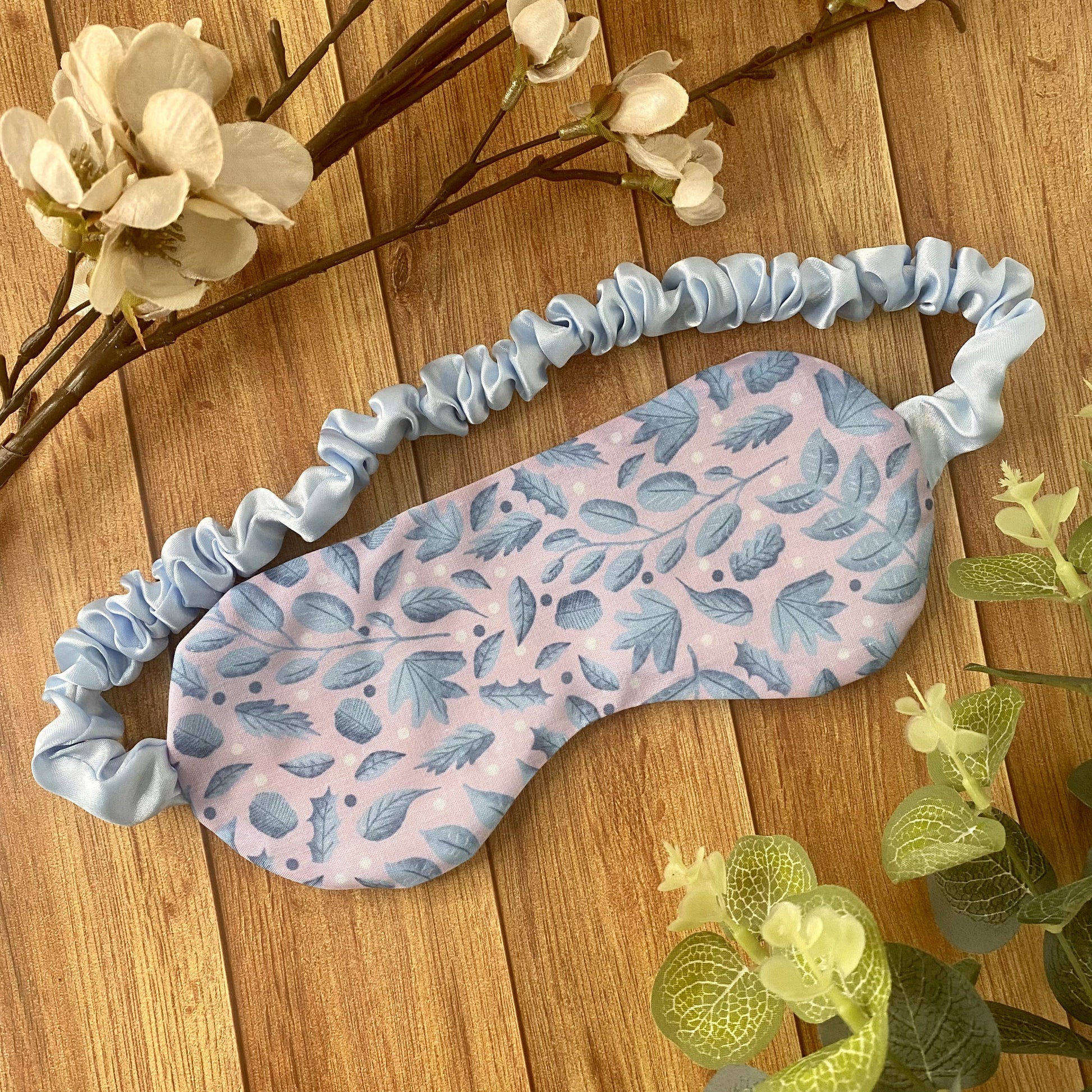 blue foliage on pink fabric made into a sleepmask, wooden background behind it