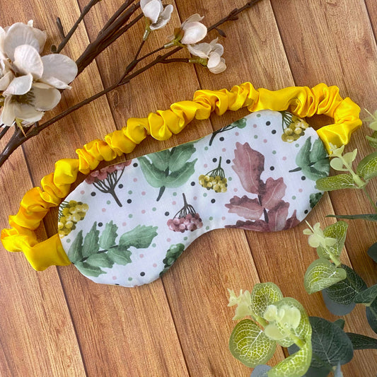 pretty foliage patterned sleepmask with a yellow scrunched strap on a wooden background
