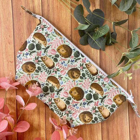 photograph of a hedgehog patterned makeup bag on a wooden background with foliage around it