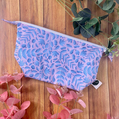 Blue and pink surface pattern design on a makeup bag gift surrounded by green and pink flowers on a wooden background