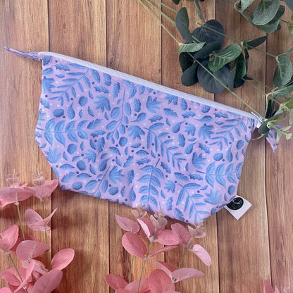 blue foliage surface pattern design on a makeup bag on a wooden background with foliage around it
