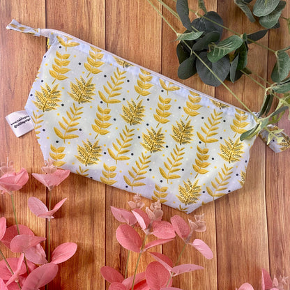 A yellow foliage patterned makeup bag on the wooden background with foliage around it