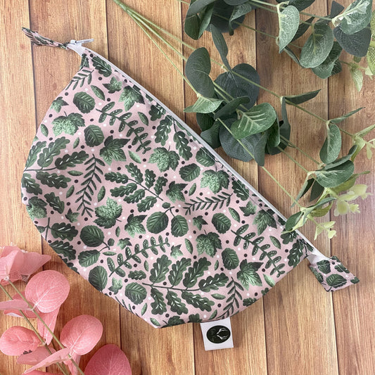 green foliage patterned makeup bag on wooden backdrop with foliage around it