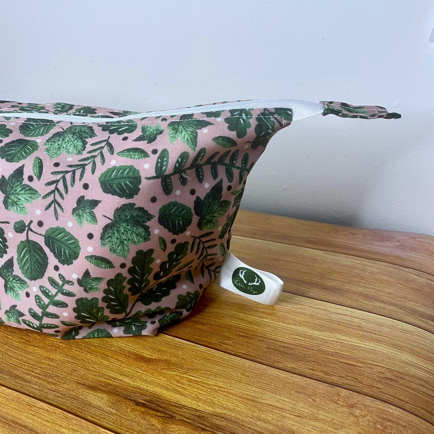 Closeup of half of the makeup bag showing the green foliage on pink pattern on a wooden background behind it
